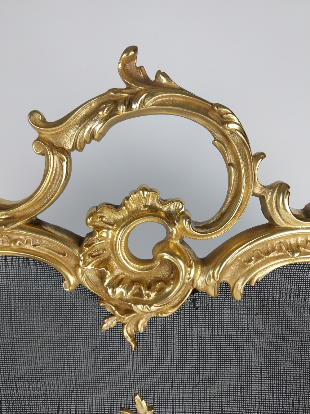 A French Louis XV style gilt bronze fire screen featuring an asymmetrical rocaille frame, central cherub motif, and woven metal mesh. View XIV