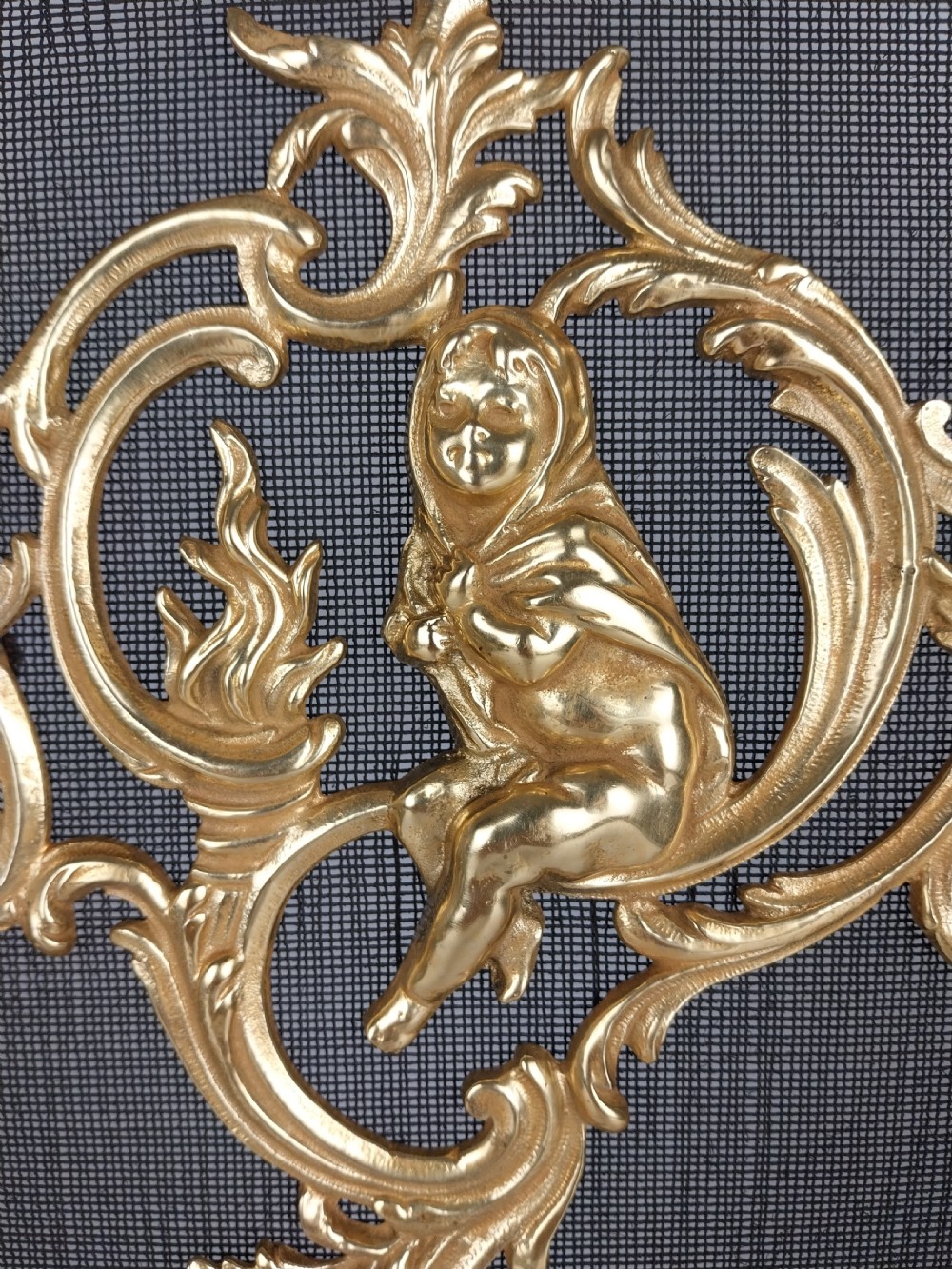 A French Louis XV style gilt bronze fire screen featuring an asymmetrical rocaille frame, central cherub motif, and woven metal mesh. View XV