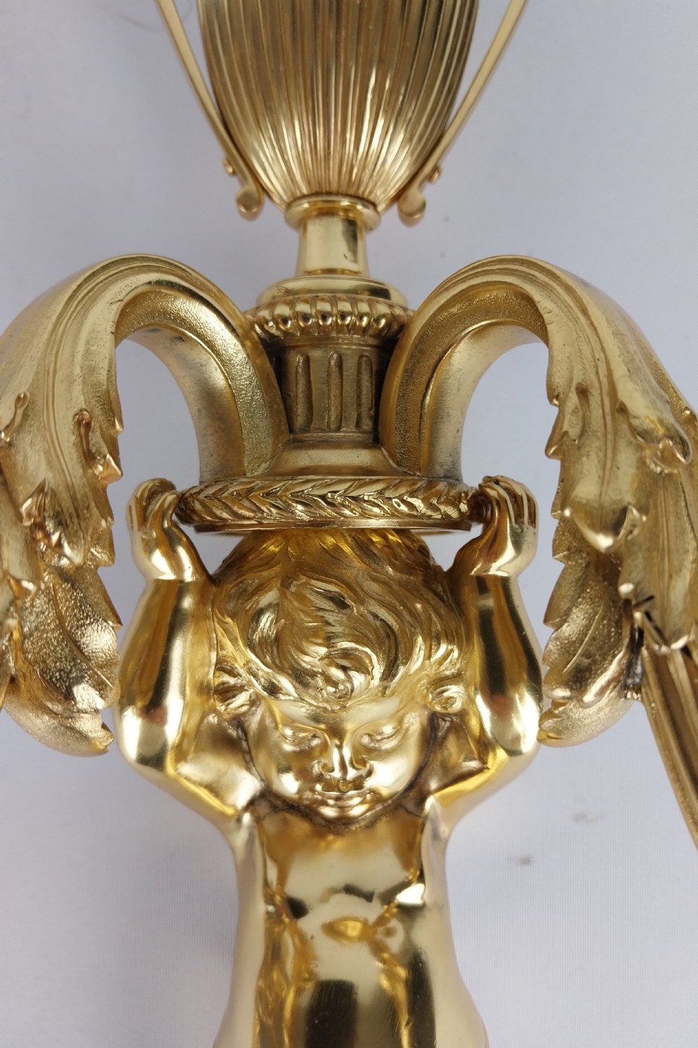 A pair of French Louis XVI style gilt bronze wall sconces featuring central cherub figures holding two curving candle arms topped with urn finials. View II