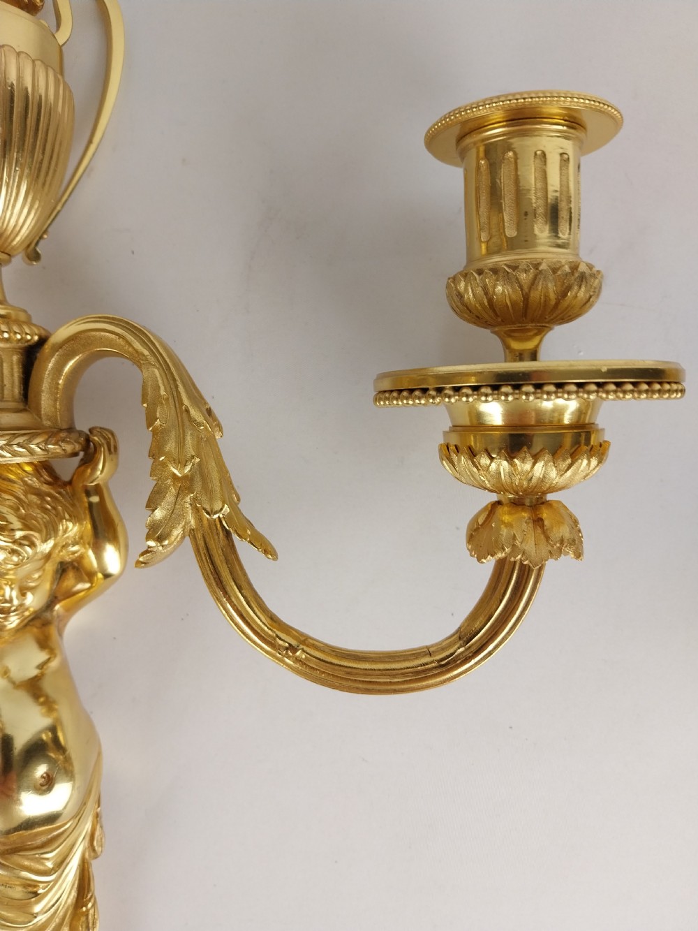 A pair of French Louis XVI style gilt bronze wall sconces featuring central cherub figures holding two curving candle arms topped with urn finials. View III