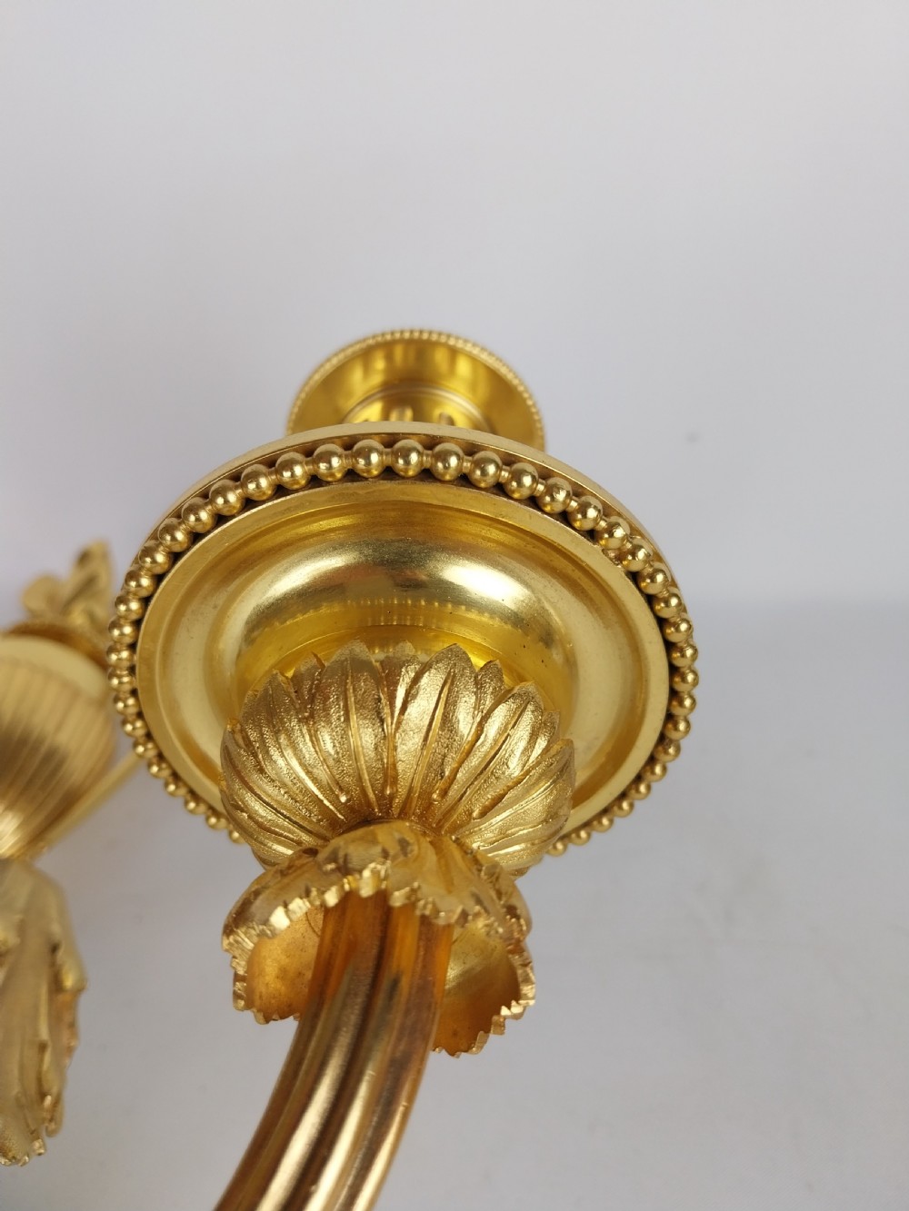 A pair of French Louis XVI style gilt bronze wall sconces featuring central cherub figures holding two curving candle arms topped with urn finials. View V