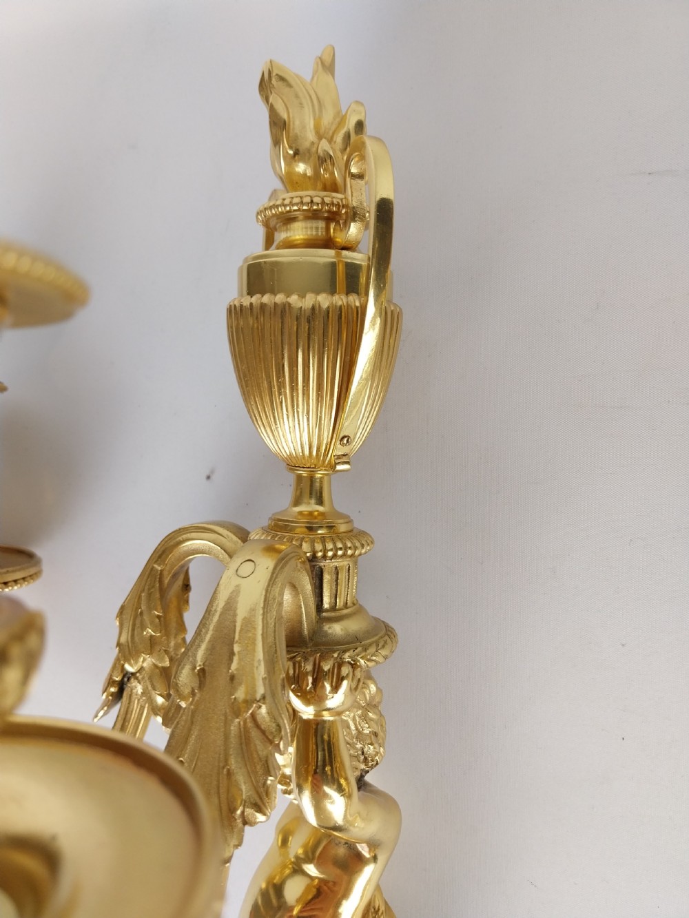 A pair of French Louis XVI style gilt bronze wall sconces featuring central cherub figures holding two curving candle arms topped with urn finials. View VII