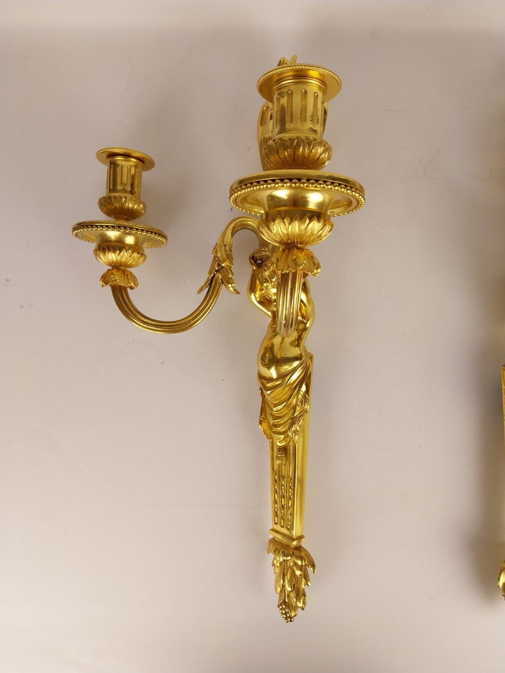 A pair of French Louis XVI style gilt bronze wall sconces featuring central cherub figures holding two curving candle arms topped with urn finials. View VIII