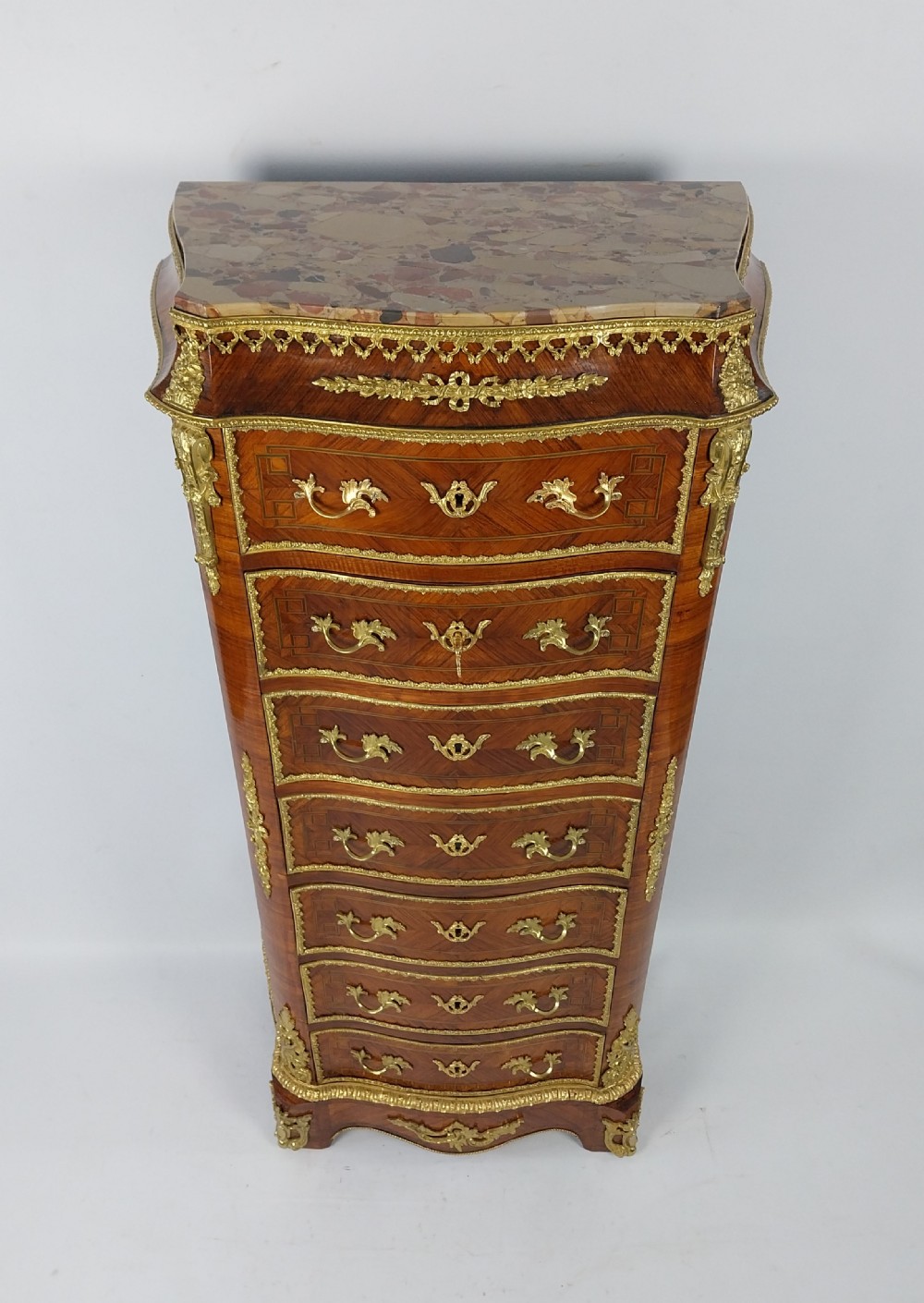 A tall 19th-century French semainier chest of drawers featuring wood marquetry veneer, ornate gilt bronze mounts, seven stacked drawers, and a marble top. View VI