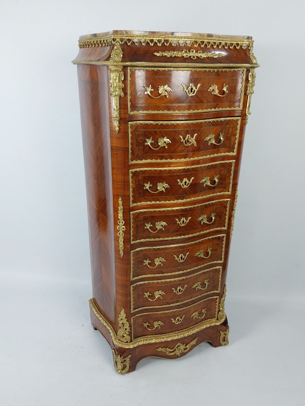A tall 19th-century French semainier chest of drawers featuring wood marquetry veneer, ornate gilt bronze mounts, seven stacked drawers, and a marble top. View XI