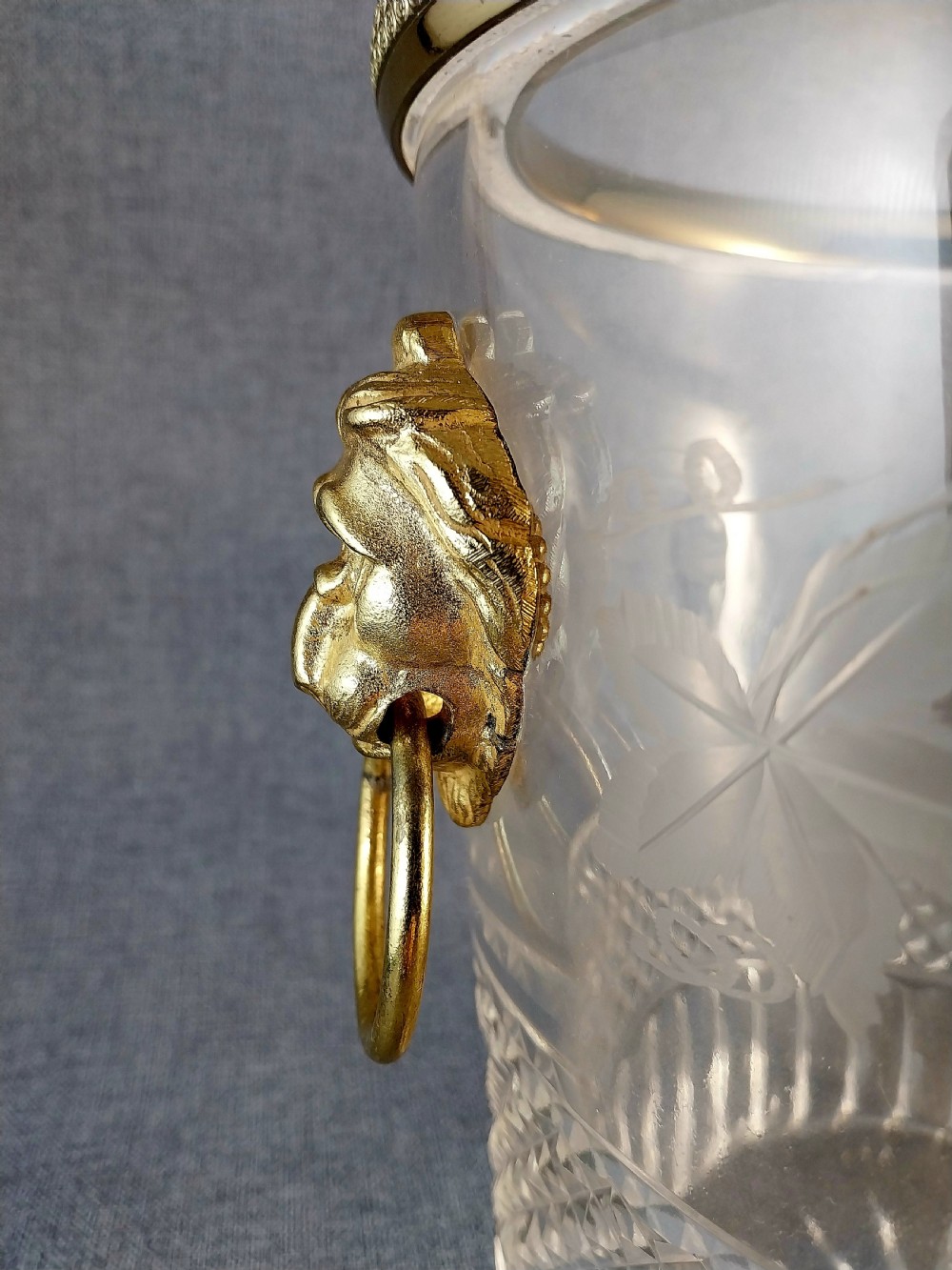 A clear cut glass champagne cooler with etched grapevine detailing, diamond-faceted lower glass, and gilt bronze lion-head ring handles. View X