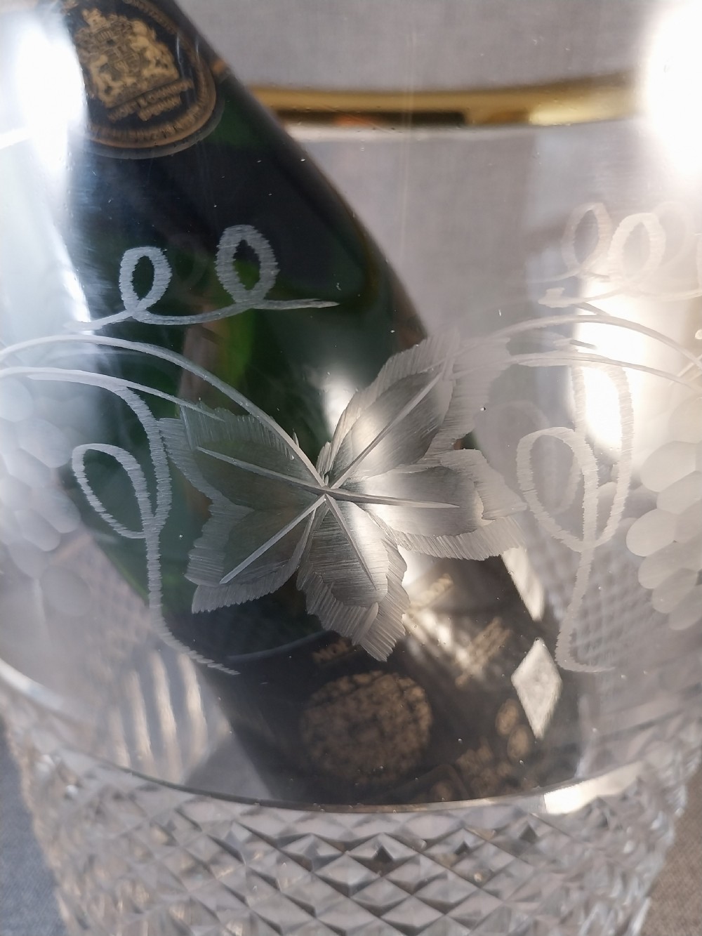 A clear cut glass champagne cooler with etched grapevine detailing, diamond-faceted lower glass, and gilt bronze lion-head ring handles. View XVI