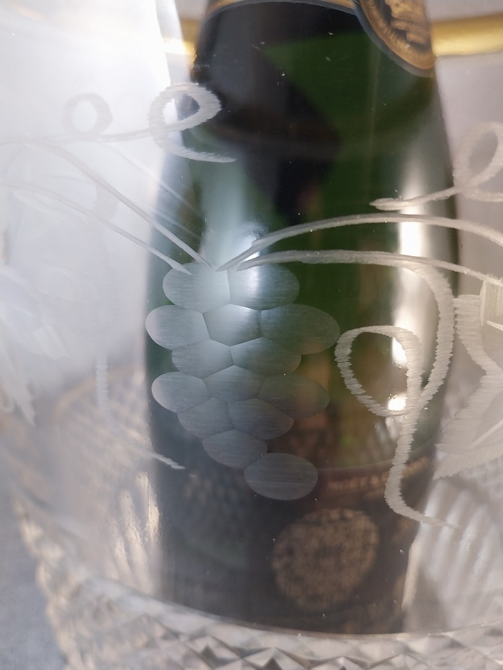 A clear cut glass champagne cooler with etched grapevine detailing, diamond-faceted lower glass, and gilt bronze lion-head ring handles. View XVII