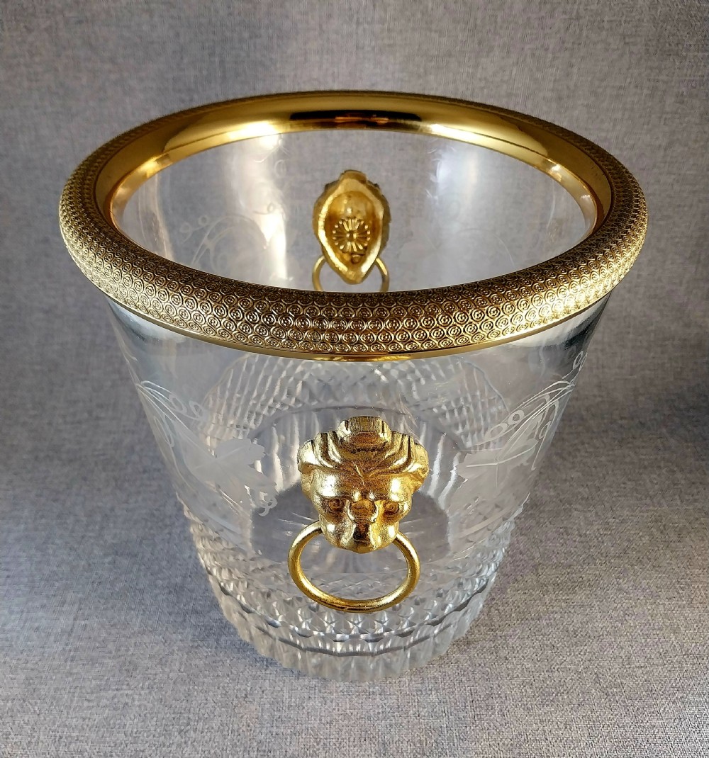 A clear cut glass champagne cooler with etched grapevine detailing, diamond-faceted lower glass, and gilt bronze lion-head ring handles. View XXV