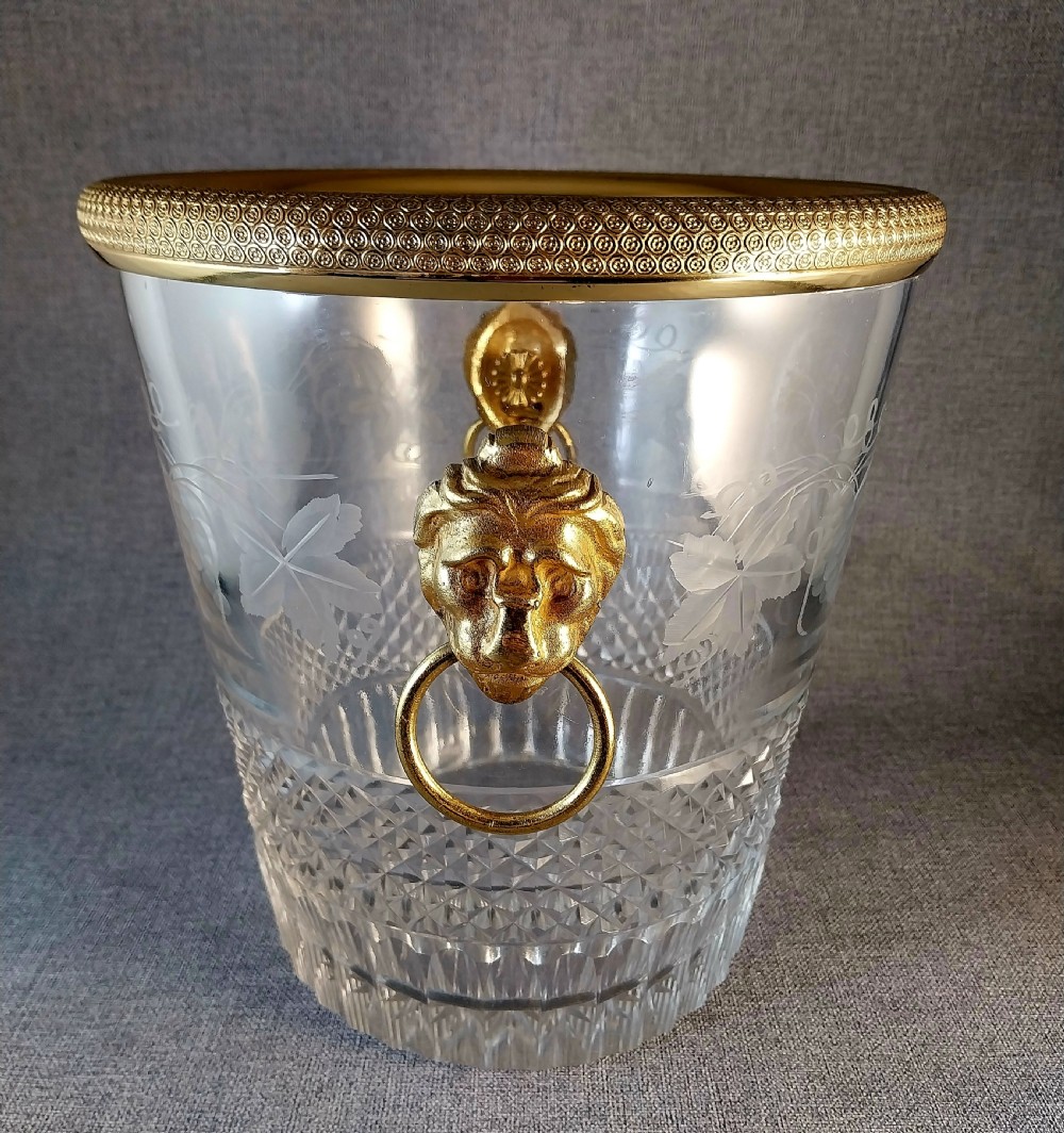 A clear cut glass champagne cooler with etched grapevine detailing, diamond-faceted lower glass, and gilt bronze lion-head ring handles. View XXVI