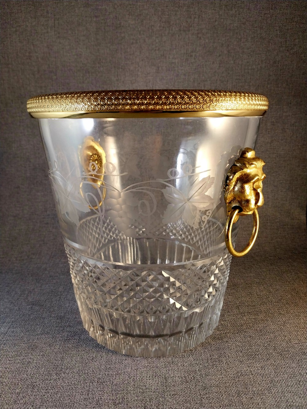 A clear cut glass champagne cooler with etched grapevine detailing, diamond-faceted lower glass, and gilt bronze lion-head ring handles. View XXVIII