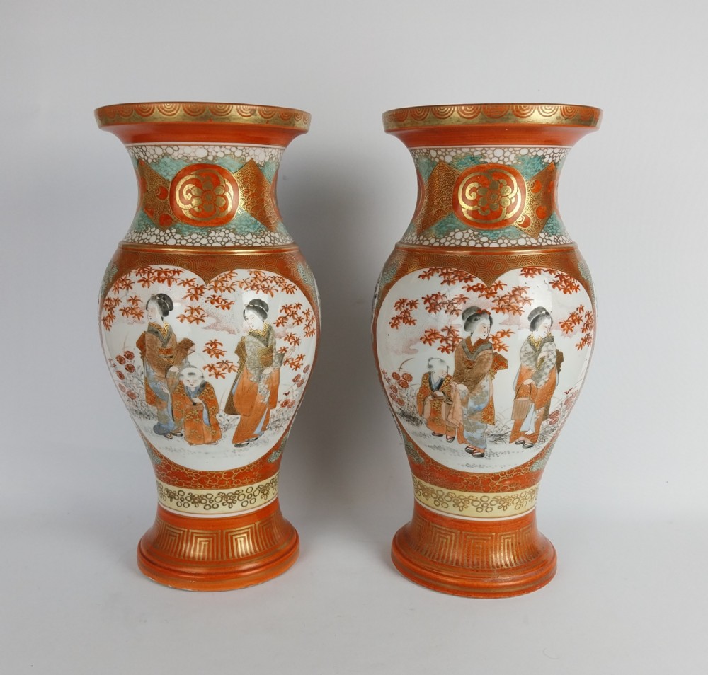 A matching pair of Japanese Kutani porcelain vases featuring baluster shapes decorated with hand-painted figure cartouches, iron-red enamel, and intricate gilt geometric borders.