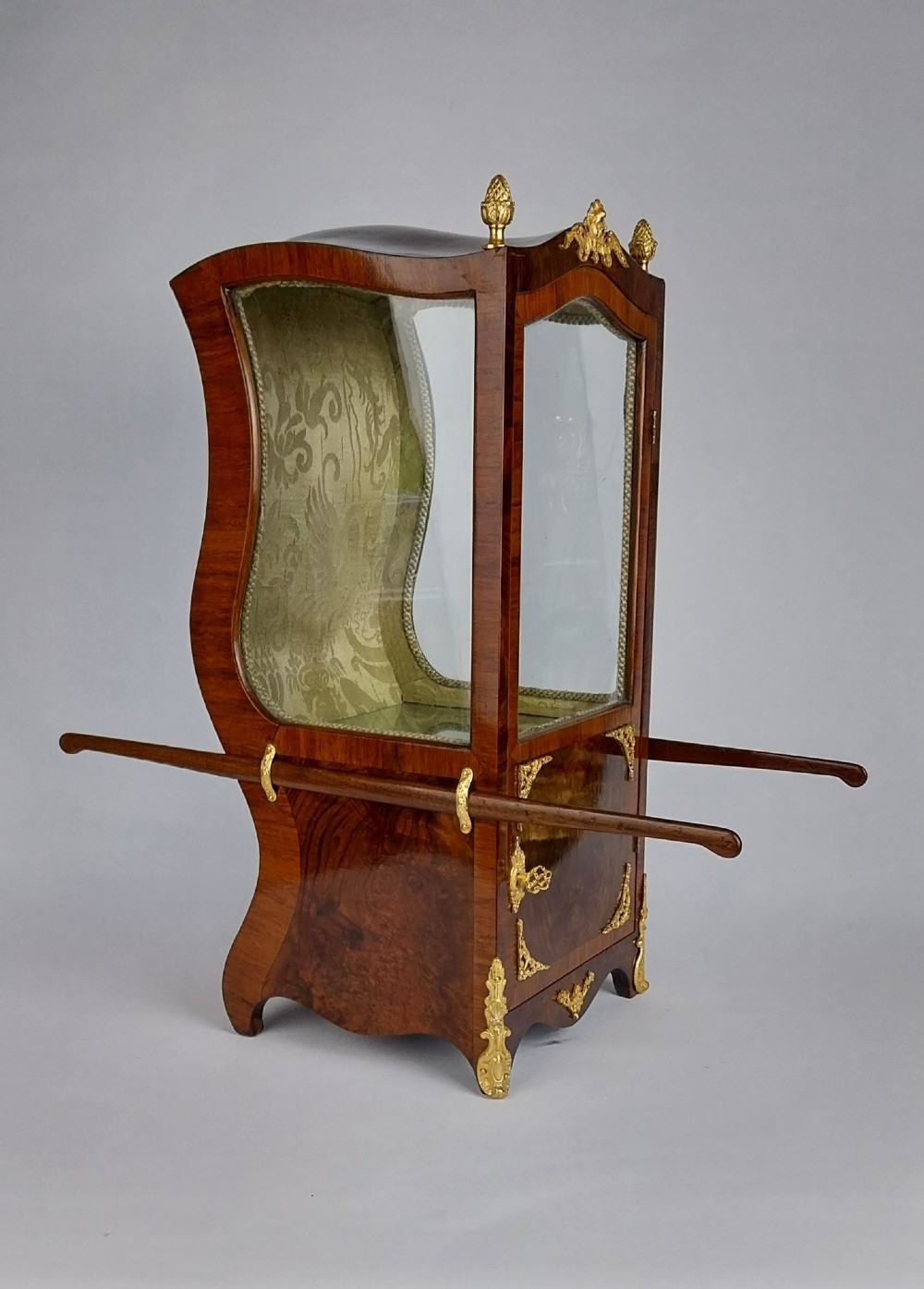 A French tabletop sedan chair vitrine cabinet crafted from polished brown wood veneer with gilt-bronze mounts, glazed side panels, removable carrying poles, and a silk damask interior. View II