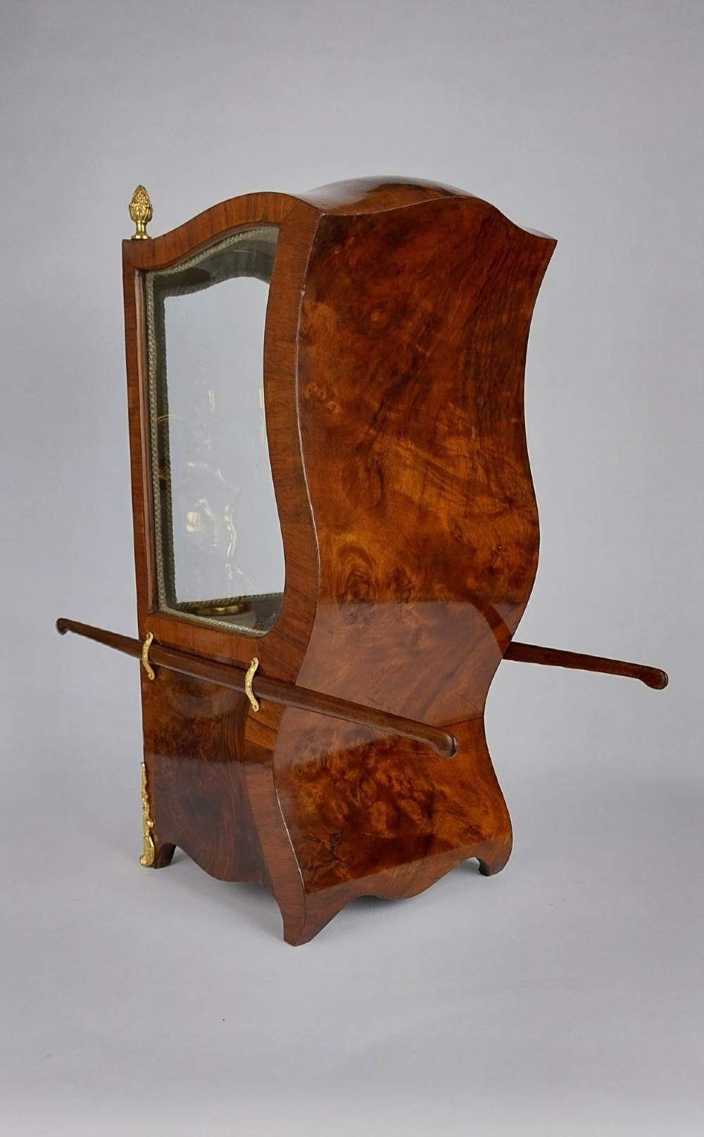 A French tabletop sedan chair vitrine cabinet crafted from polished brown wood veneer with gilt-bronze mounts, glazed side panels, removable carrying poles, and a silk damask interior. View V