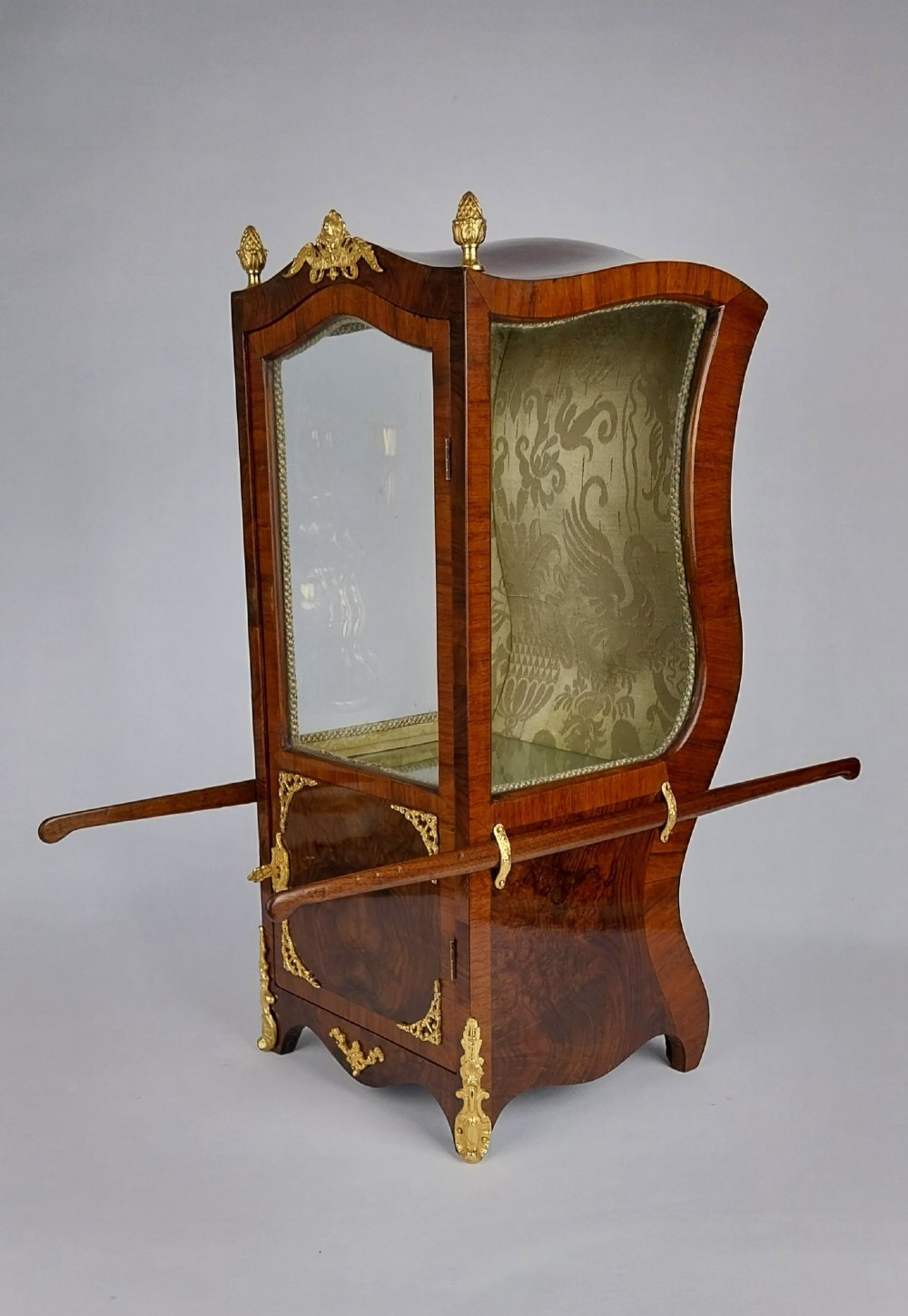 A French tabletop sedan chair vitrine cabinet crafted from polished brown wood veneer with gilt-bronze mounts, glazed side panels, removable carrying poles, and a silk damask interior. View VII