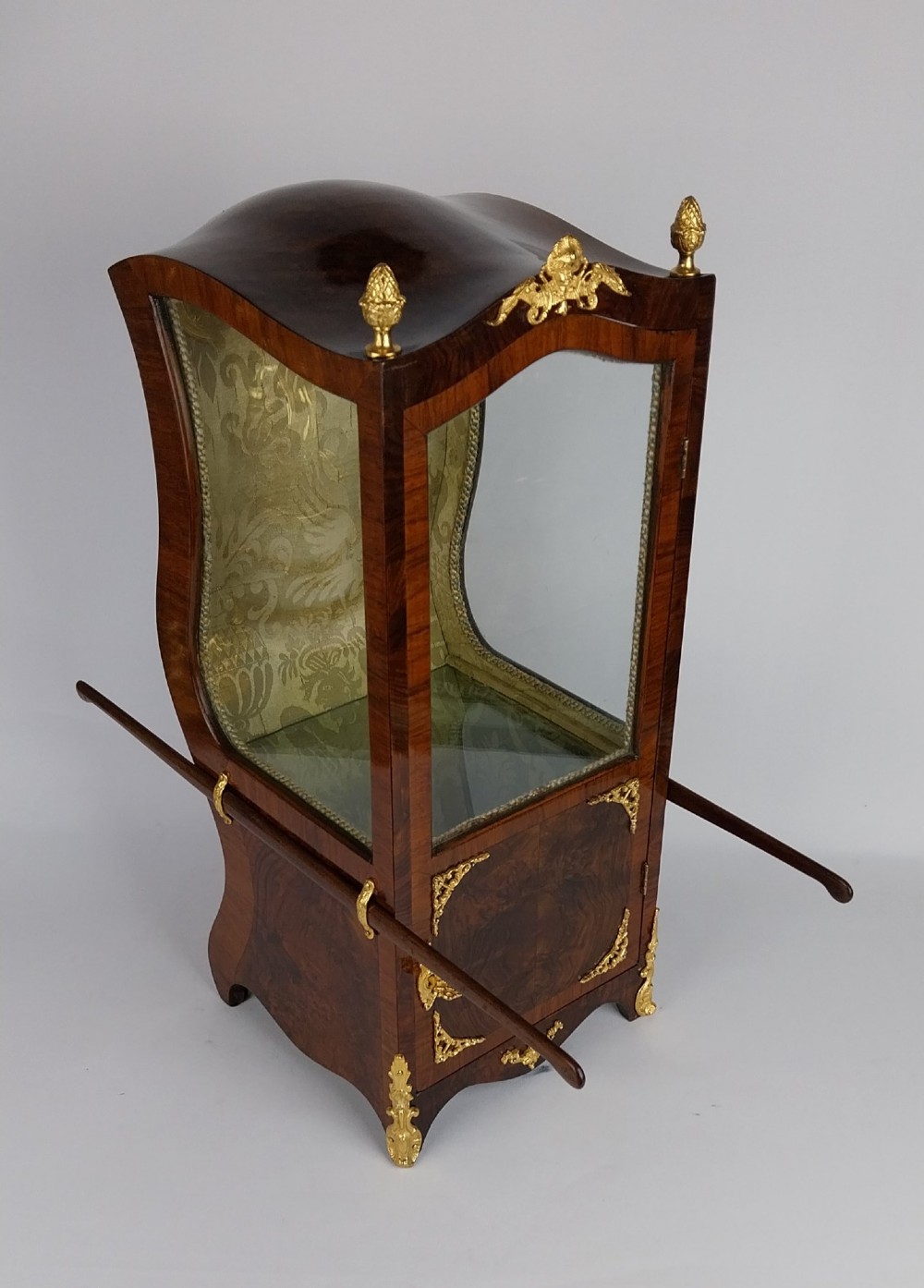 A French tabletop sedan chair vitrine cabinet crafted from polished brown wood veneer with gilt-bronze mounts, glazed side panels, removable carrying poles, and a silk damask interior. View IX