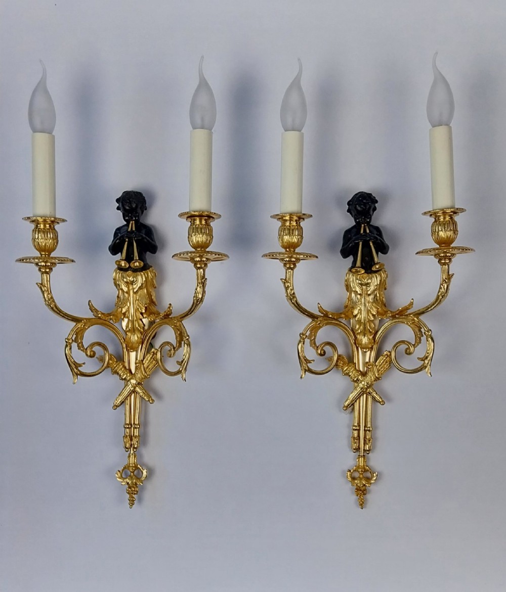 A pair of French gilt and dark patinated bronze two-branch wall sconces featuring central figures holding musical instruments.