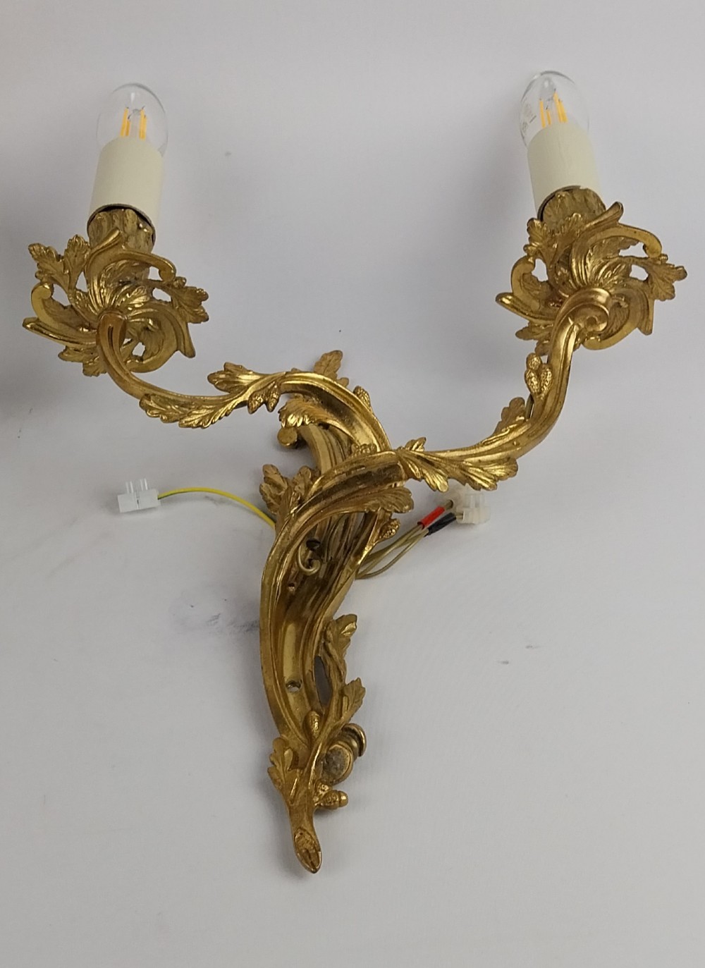 A pair of French Rococo style gilt bronze two-arm wall sconces featuring scrolling acanthus leaf backplates and candle-style sockets. View V