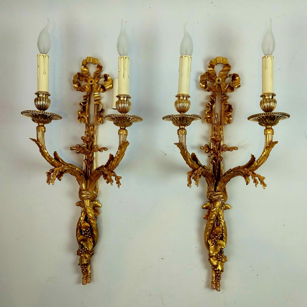A pair of antique French gilt bronze two-arm wall sconces decorated with top ribbon bow crests and foliate scroll branches.
