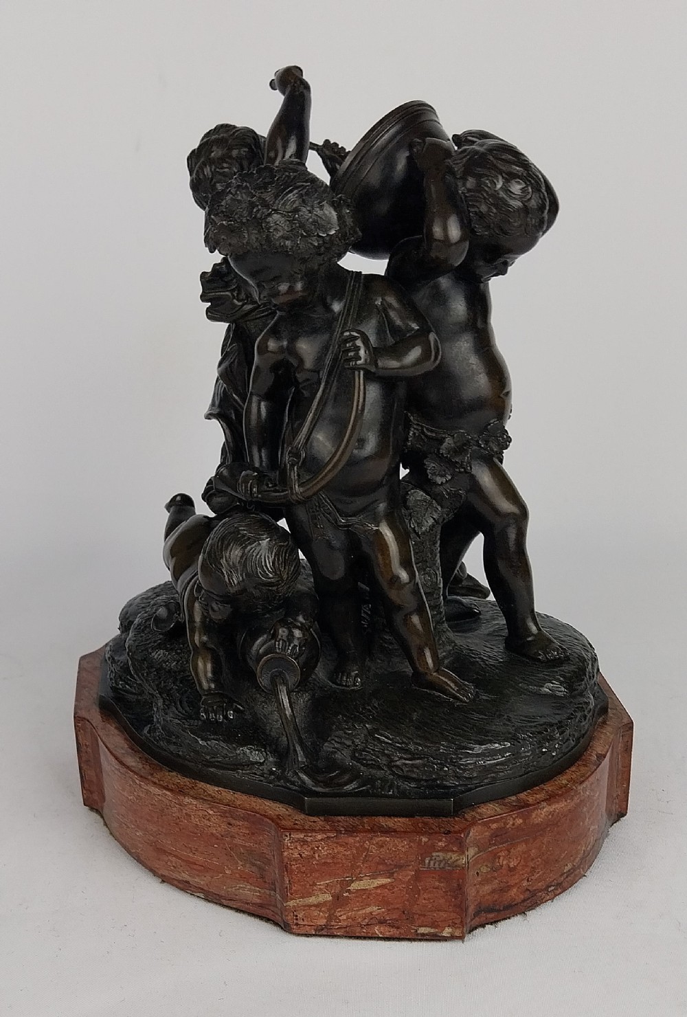 A dark patinated bronze sculptural group depicting several cherubs around a vessel on a moulded octagonal base.