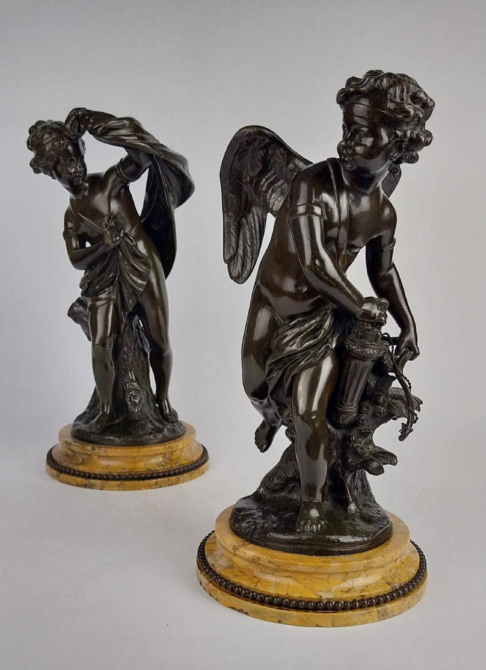 A pair of dark patinated bronze sculptures depicting the classical figures Cupid and Psyche set upon round yellow marble bases.
