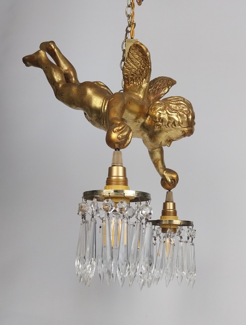 An antique gilded winged cherub hanging ceiling light fixture suspended by a chain, holding two light sockets dressed with crystal droplets.