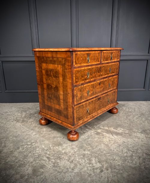 fig 2. A William and Mary period walnut chest of drawers featuring geometric oyster veneering, brass teardrop handles, and turned bun feet.