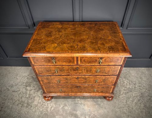 fig 3. A William and Mary period walnut chest of drawers featuring geometric oyster veneering, brass teardrop handles, and turned bun feet.