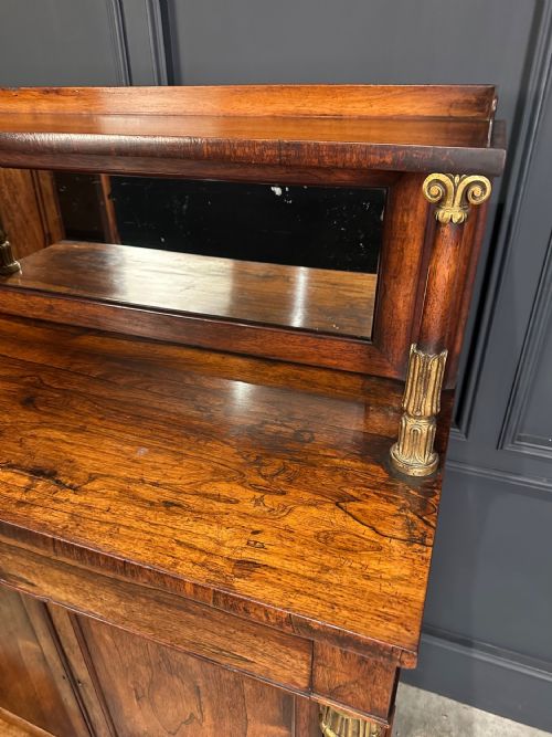 fig 1. A William IV dark rosewood chiffonier featuring a mirrored top shelf supported by gilded columns over a two-door cabinet with paw feet.