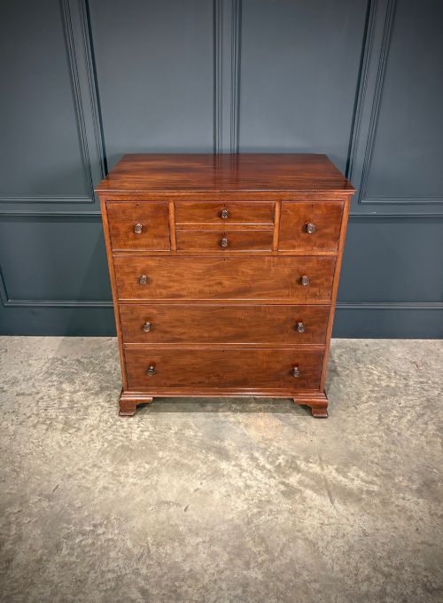 fig 2. A tall antique mahogany chest of drawers featuring an upper arrangement of small drawers over three graduated full-width drawers, resting on bracket feet.