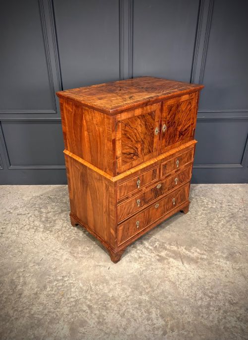 fig 1. An antique walnut cabinet on chest featuring a twin-door top cupboard over graduating drawers with brass hardware and bracket feet.