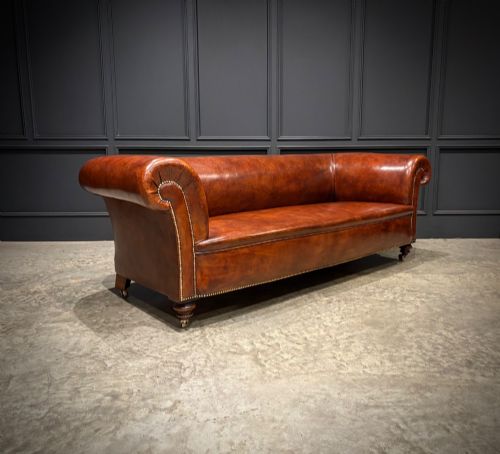 fig 1. A Victorian chestnut brown leather sofa featuring continuous rolled arms, brass studding detail, and turned wood legs on castors.