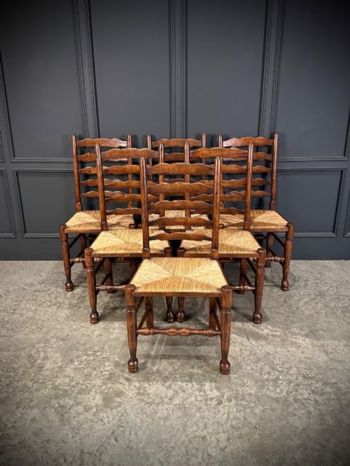 fig 1. A set of eight dark oak ladder back dining chairs featuring woven rush seats, shaped back slats, and turned front legs.