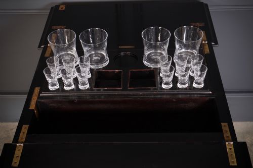 fig 3. An ebonised wooden mechanical drinks table featuring opening top leaves that elevate a tray set with clear glassware, resting on tapered legs with brass castors.