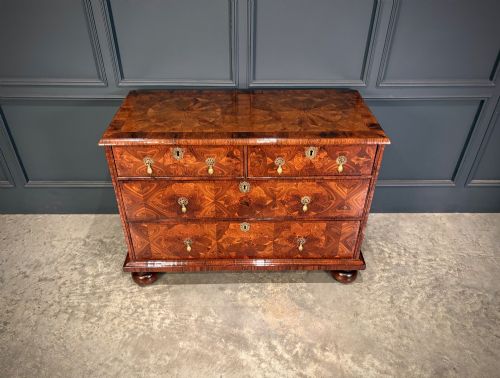 fig 2. A seventeenth-century kingwood chest of drawers featuring geometric oyster veneering, brass teardrop handles, and turned bun feet.