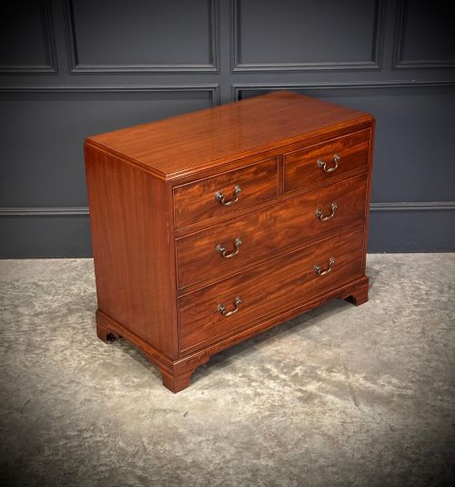 fig 1. A small mahogany chest of drawers featuring two short over two long drawers with brass swan-neck handles and bracket feet.