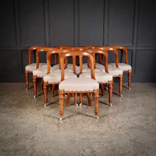 fig 1. A set of ten Victorian oak dining chairs with rounded hoop backs, neutral fabric seats with stud trim, and carved front legs on ceramic castors.