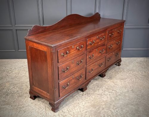 fig 1. An 18th-century mahogany bank of nine drawers featuring a shaped upstand gallery back, brass swan-neck handles, and bracket feet.