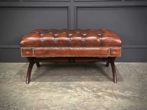 fig 1. A rectangular hand-dyed brown leather footstool with deep button tufting, brass studding, and an X-frame wooden base.