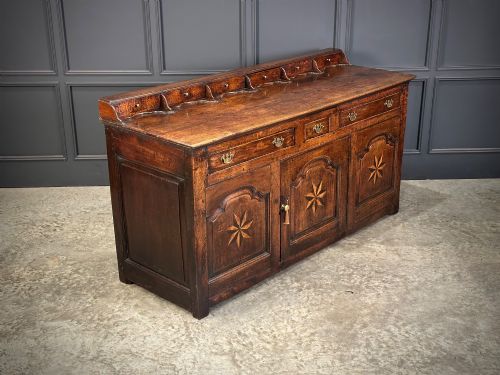 fig 1. An 18th-century dark oak dresser base featuring three main drawers over three arched cupboard doors with star inlay details and brass handles.