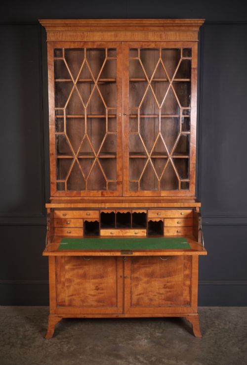 fig 3. A tall Georgian satinwood secretaire bookcase featuring an upper glazed cabinet with geometric astragal bars, a fold-down desk drawer, and a lower double-door cupboard on splayed bracket feet.