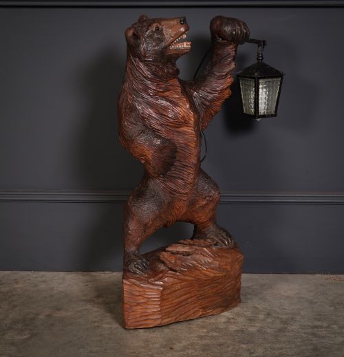 fig 1. A dark hand-carved timber standing bear sculpture holding an iron lantern light fixture on a textured wooden base.