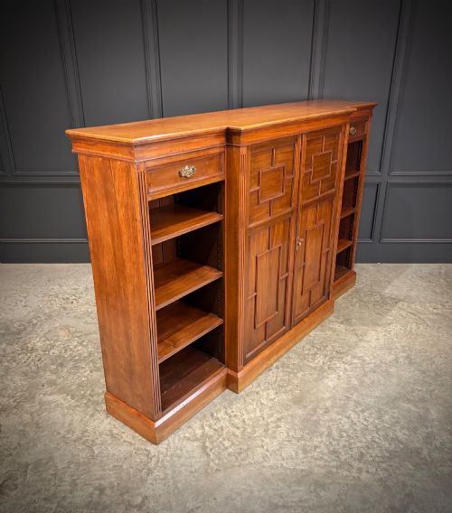 fig 1. An antique Edwardian walnut breakfront bookcase with a central section featuring geometric panelled doors flanked by open adjustable shelving.