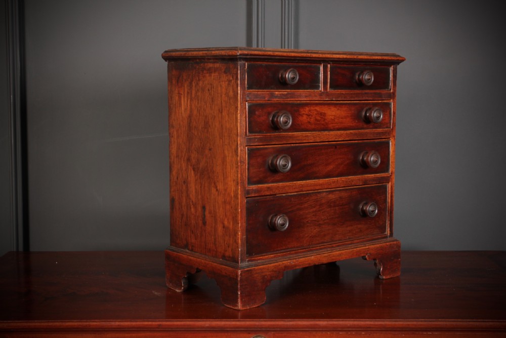 A Georgian style miniature mahogany chest of drawers with two short drawers over three long graduated drawers, turned knobs, and bracket feet.