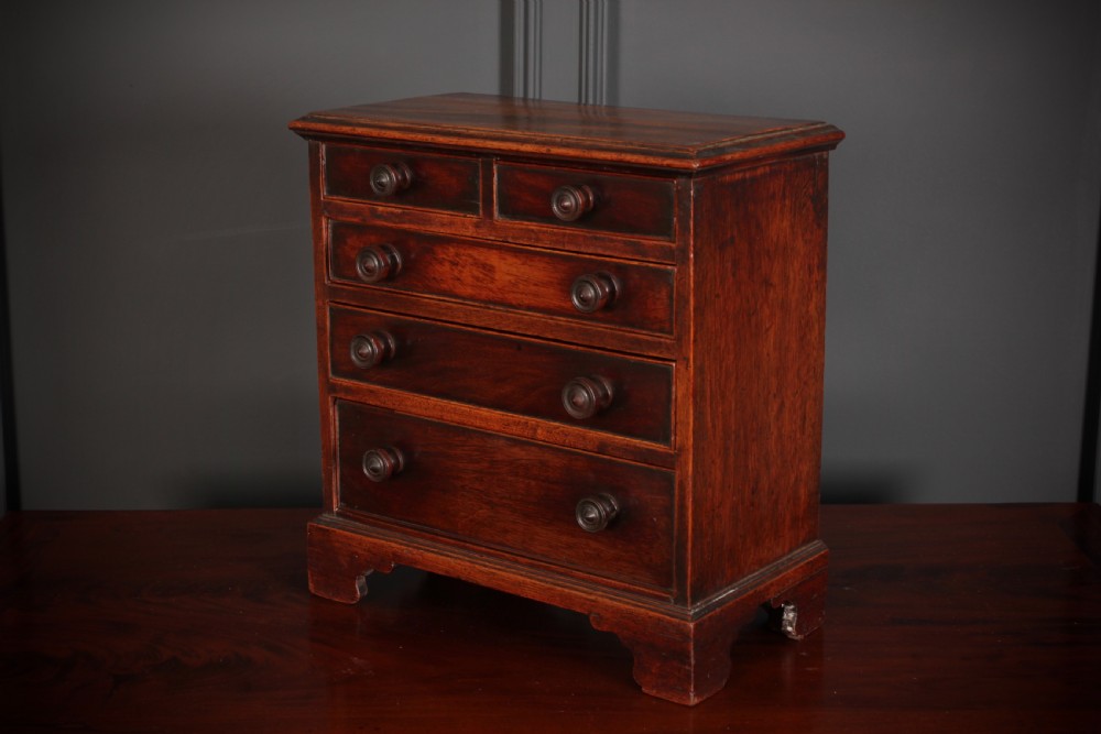 A Georgian style miniature mahogany chest of drawers with two short drawers over three long graduated drawers, turned knobs, and bracket feet. View V