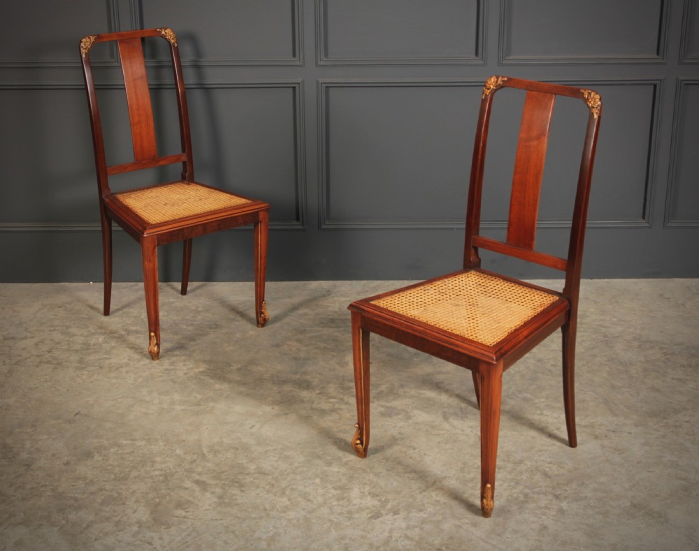 A pair of polished walnut bedroom chairs with woven cane seats, central splat backs, and carved gilt accents at the top corners and feet. View II