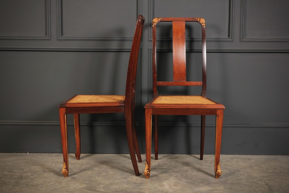 A pair of polished walnut bedroom chairs with woven cane seats, central splat backs, and carved gilt accents at the top corners and feet. View VI