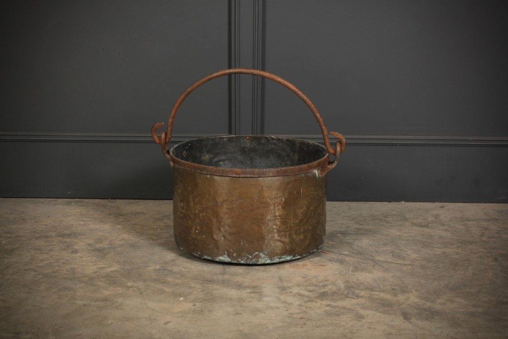 A large, hand-hammered Victorian brass cauldron featuring an iron rim collar and a heavy wrought iron swing handle.