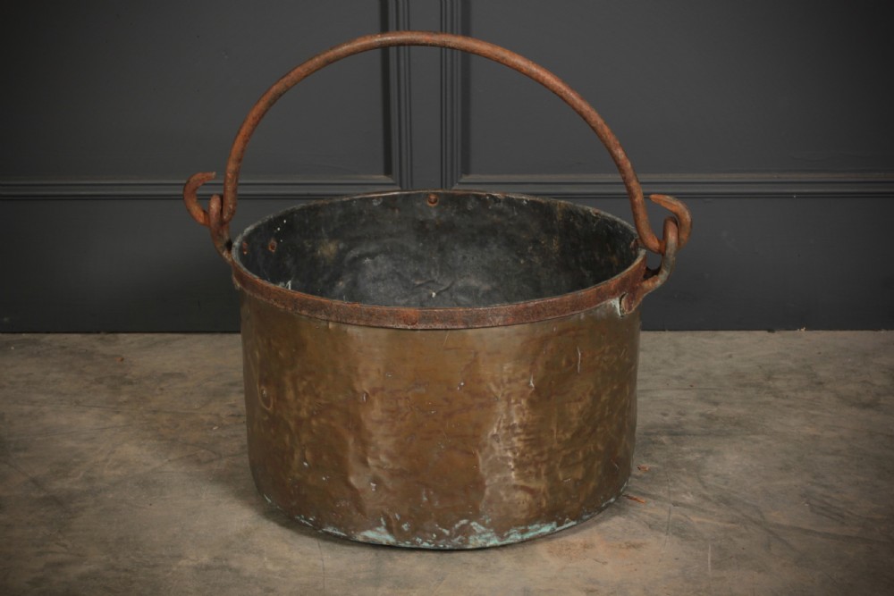 A large, hand-hammered Victorian brass cauldron featuring an iron rim collar and a heavy wrought iron swing handle. View II