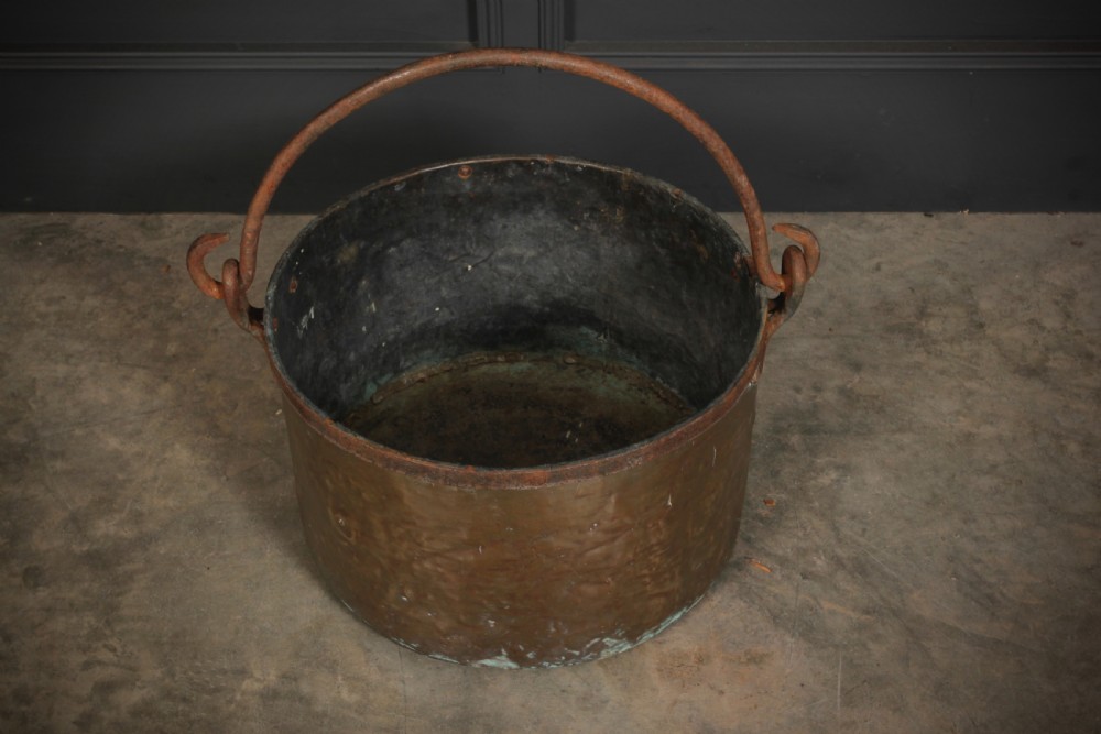 A large, hand-hammered Victorian brass cauldron featuring an iron rim collar and a heavy wrought iron swing handle. View IV